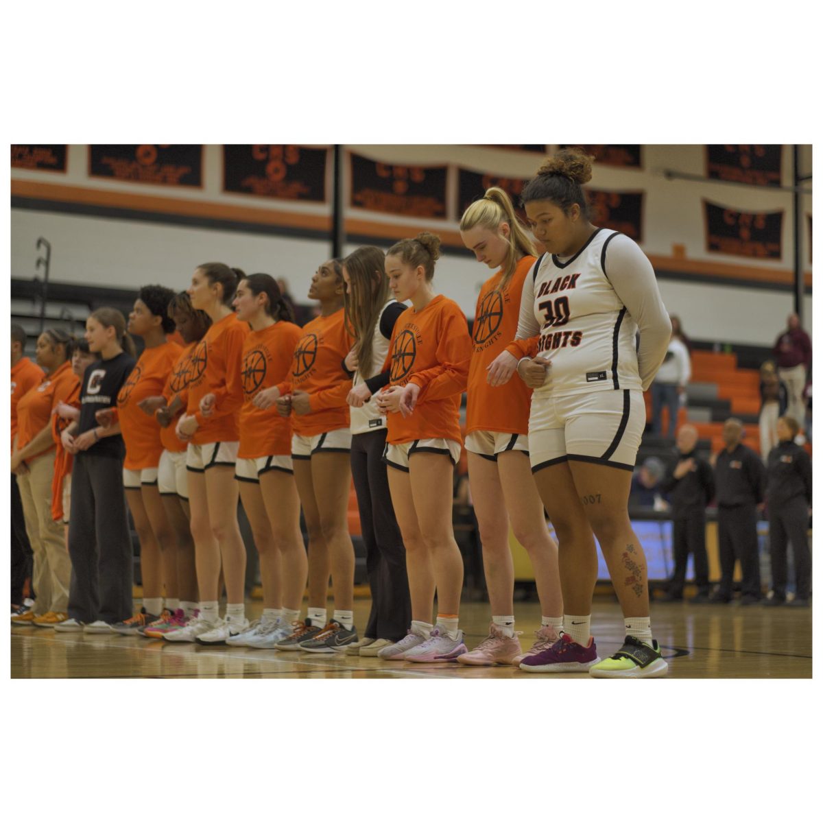 The girls basketball team listening to the national anthem.